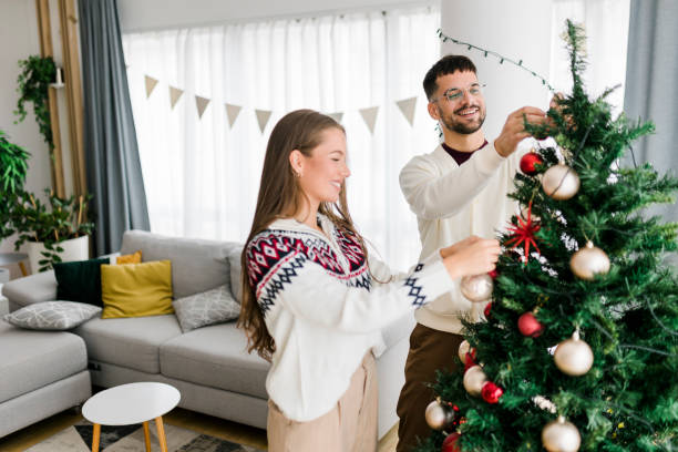 istock Happy young couple wearing sweaters having fun decorating various baubles on the Christmas tree in the living room at home. Enjoying and celebrating the Christmas holiday. 1431919400