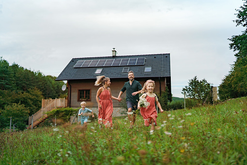 Happy family running near their house with a solar panels. Alternative energy, saving resources and sustainable lifestyle concept.