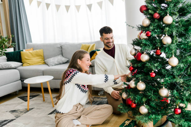 istock Happy young couple wearing sweaters having fun decorating various baubles on the Christmas tree in the living room at home. Enjoying and celebrating the Christmas holiday. 1431920741