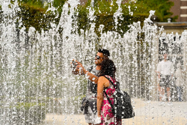 Amsterdam, Netherlands - August 2022: Two people taking a selfie while standing in the middle of a fountain in a public garden