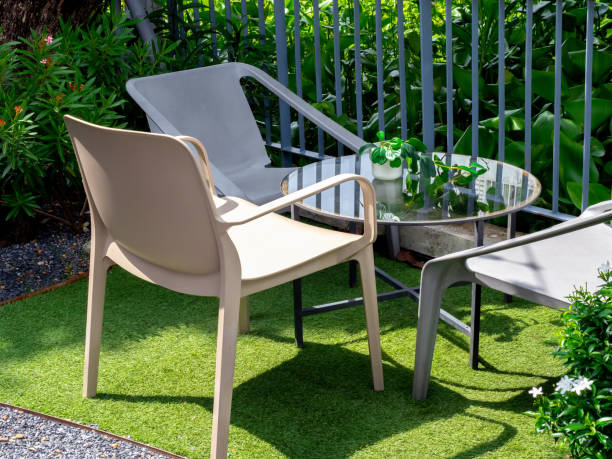istock Three empty beige plastic chairs with round glass table with small plant pot in the outdoor garden on artificial grass floor and grey iron fence. Table set relaxing in garden. 1431928083