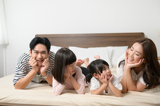 A Portrait of asian Parents with two little daughters on the bed in bedroom, happy family concept