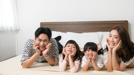 A Portrait of asian Parents with two little daughters on the bed in bedroom, happy family concept