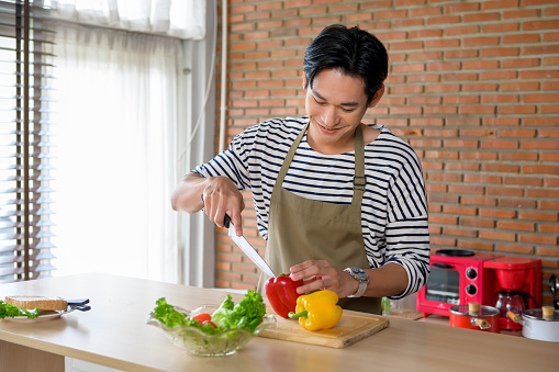 A Young smiling asian man wearing an apron in the kitchen room, cooking concept