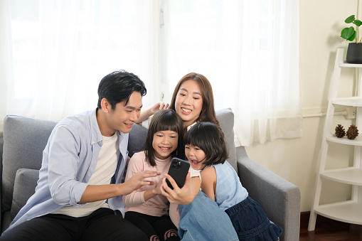 An Asian family with children holding smartphone and making video call at home