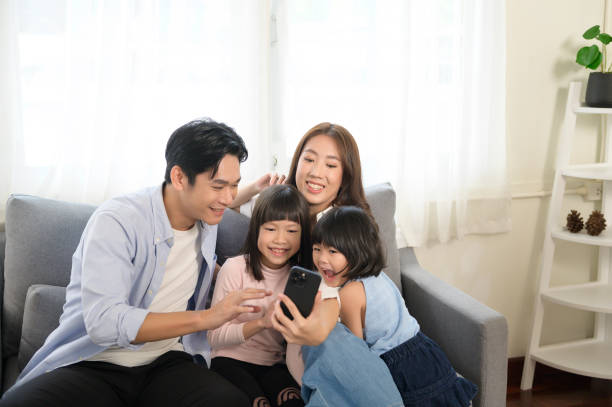 Asian family with children holding smartphone and making video call at home stock photo