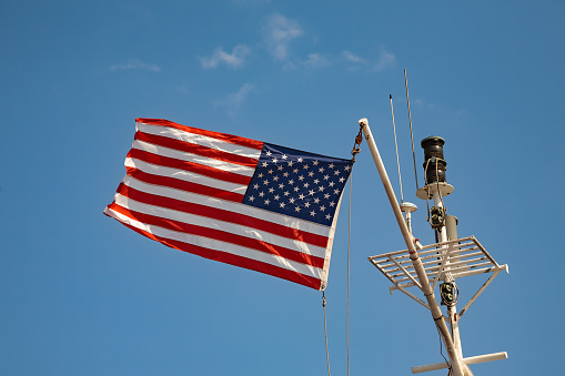 United States of America stars and stripes flag flying against a blue sky on top of a boat mast.