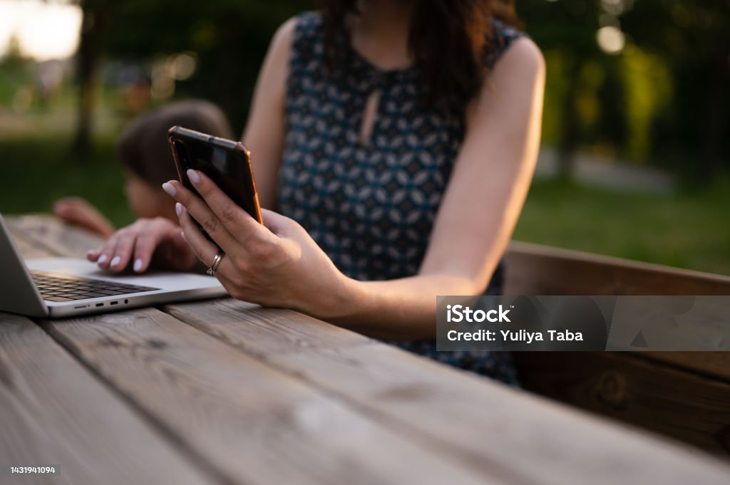 beautiful business woman working on a laptop sitting on the bench in a park in the evening. Online training, remote work and communication in social networks.woman working and typing on laptop keyboard and using smartphone while sitting in the park. young woman working on laptop in the park in the evening 30-34 Years Stock Photo