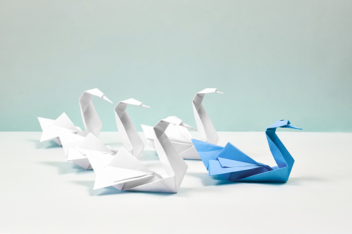 A blue swan leads a flock of white swans. Paper swans on a blue background. Origami.