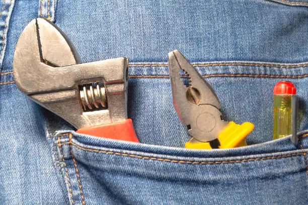 Photo of Tools in the pocket of blue jeans - pliers and screwdrivers.