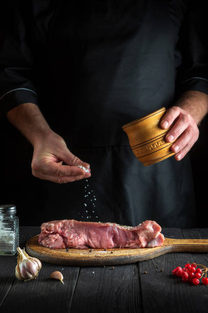 le chef prépare de la viande de veau crue. avant la cuisson, le chef ajoute du sel au bœuf. le plat national est préparé dans la cuisine du restaurant - veal calf meat baking photos et images de collection