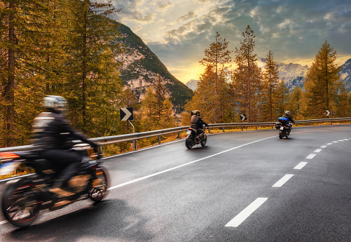 Travel concept. Group of people travelers on motorcycles ride on an asphalt road in the mountains at sunset in the Italian Alps. Beautiful autumn landscape