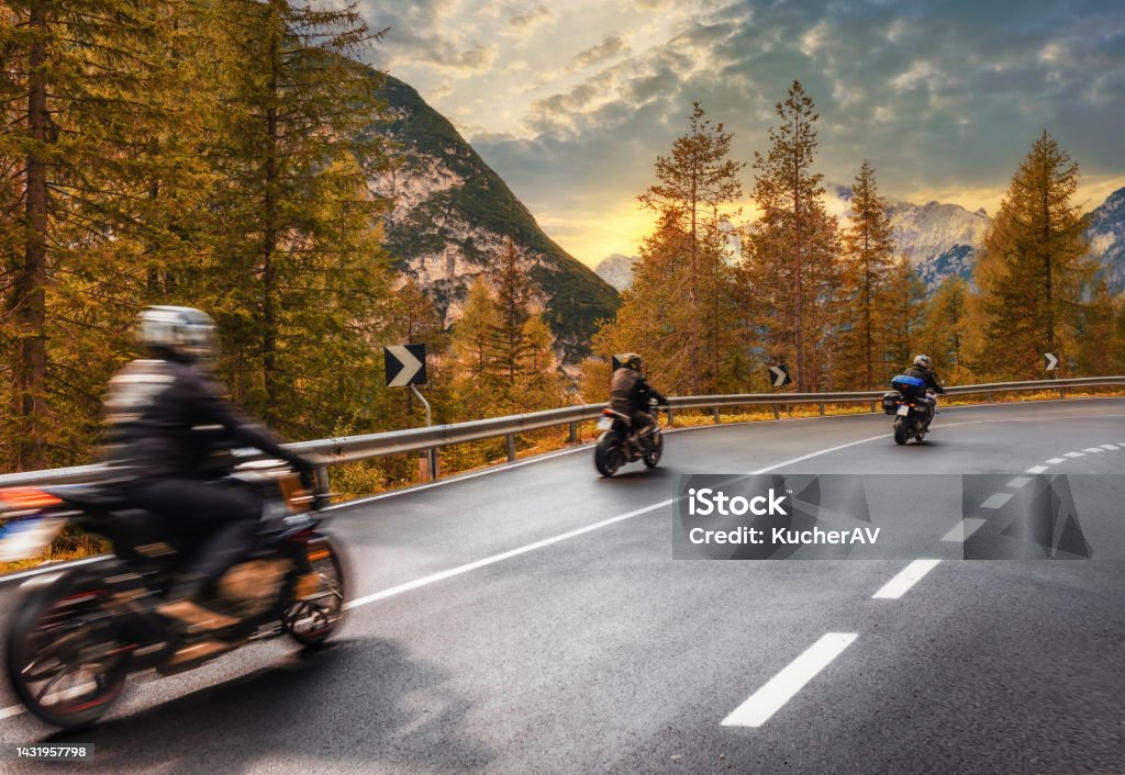 Travel concept. Group of people travelers on motorcycles ride on an asphalt road in the mountains at sunset in the Italian Alps Beautiful autumn landscape Travel concept. Group of people travelers on motorcycles ride on an asphalt road in the mountains at sunset in the Italian Alps. Beautiful autumn landscape Motorcycle Stock Photo