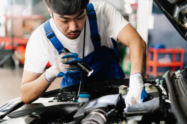 istock Asian Mechanic working and checking engine in garage, Professional technician is wearing gloves and shine a flashlight on the car, Car Service and Automobile Maintenance Concept 1431962720
