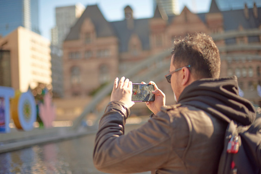 Toronto Ontario, Canada- October 3rd, 2022: A man taking a photo of Toronto City Hall with his iPhone.