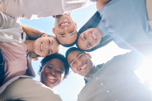 istock Diverse group of friends in a huddle together showing unity, trust and support outdoors in summer from below. International, happy and young men and women smiling, united and cheerful team outside 1431968603