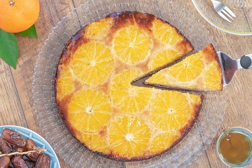 Homemade whole testy vanilla orange date upside down cake made from almond meal, eggs, dates and orange slices on the top and a drizzle orange syrup