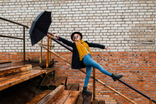 A woman in autumn clothes with a black umbrella flies away from a gust of wind. The concept of bad weather.