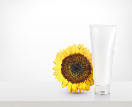 Cosmetic plastic tube and with sunflowers on table white background