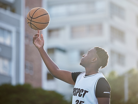 Basketball player, athlete and sports man with skill spinning a ball on his finger during training for game, match or competition outdoor. Black man with motivation, goal and mindset prepared to win