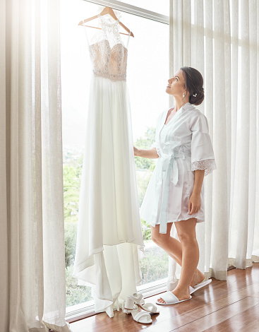 Wedding, bride and married with a woman looking at a dress before her marriage ceremony or celebration event. Love, romance and matrimony with an attractive young female getting ready in a room