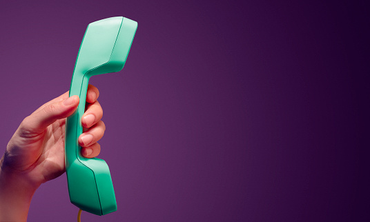 A female hand holding vintage colorful corded phone on a purple background. Communication concept in 90's colors