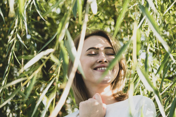 istock Cute woman smiling under willow tree in sunlight with shadow from branches. Female portrait in woodland on sunny day. 1431976082