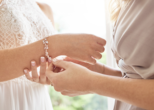 Wedding bride and bridesmaid help with jewellery bracelet for elegant and classic fashion glamour. Expensive bridal diamond accessory for classy style at special ceremony event day closeup.