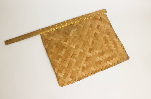 Woven bamboo hand fan on grey background. A traditional utensil often used by satay seller in Indonesia to keep the wood charcoal on fire, when grilling satay. An eco-friendly tool. Medium close up. abanico de mano de bambú tejido sobre fondo gris. un utensilio tradicional utilizado a menudo por el vendedor de satay en indonesia para mantener el carbón de leña en el fuego, al asar satay. una herramienta ecológica. primer plano medio.
