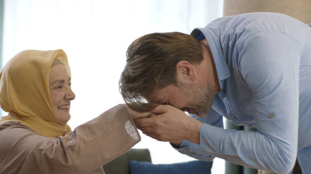 The young man is visiting his elderly mother on a special day. Young man kisses his mother's hand during Eid Mubarak (Turkish Ramadan or Şeker Bayram).The man kisses her hand to show respect to her veiled mother.Muslim holiday traditions concept. father allah stock pictures, royalty-free photos & images