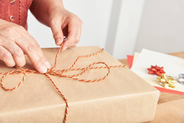 mains d’une femme mûre inconnue attachant un cadeau de noël avec une ficelle décorative - wrapped package string box photos et images de collection