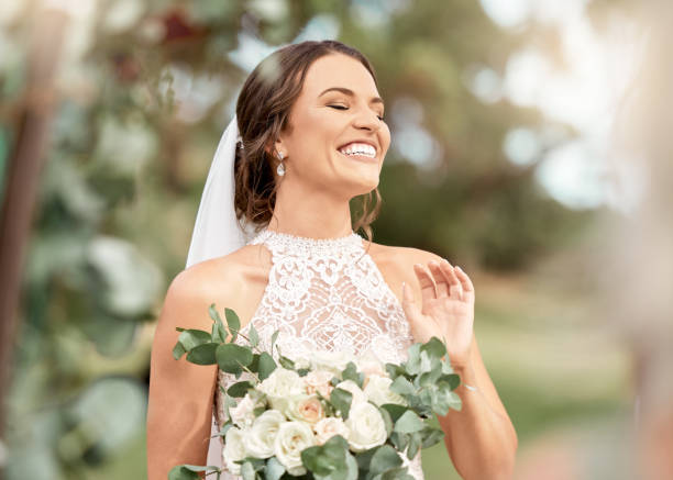 aufgeregte braut in hochzeit mit blumenstrauß im naturpark mit grünen bäumen, bokeh und sommersonne. glück, engagement und traum einer schönheitsfrau mit blumen für die ehe im freien lens flare - braut stock-fotos und bilder