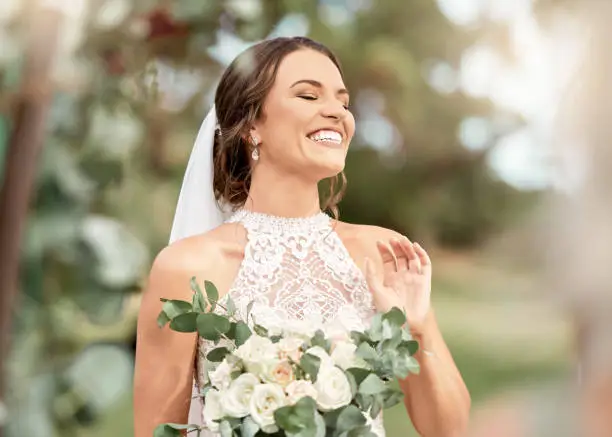 Photo of Excited bride in wedding with bouquet in nature park with green trees, bokeh and summer sunshine. Happiness, commitment and dream of a beauty woman with flowers for marriage in outdoor lens flare