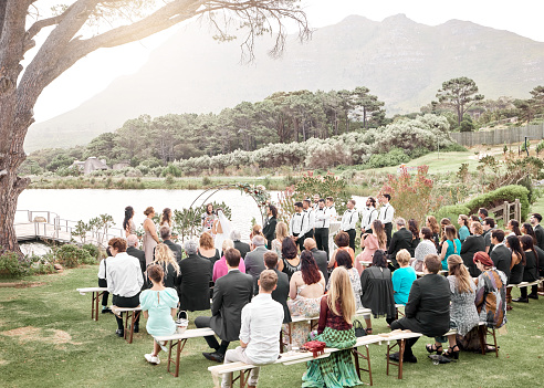 Wedding, nature and guests sitting at the ceremony in a lake garden for marriage celebration. Love, outdoors and friends and family watching a couple get married at a luxury, elegant and happy event.