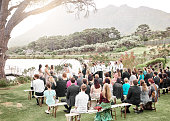 Wedding, nature and group of family and friends at the ceremony in a lake garden for celebration. Love, outdoors and guests watching a couple get married at a luxury, elegant and marriage event.