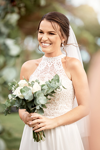 Bride excited with flowers in hands, smile on spring wedding day in dress and veil. Woman getting married, show happiness and nerves outdoors with bouquet of roses and leaves in green garden