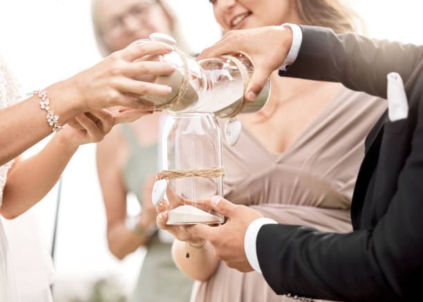 Couple, wedding and glasses of sand, for ceremony or symbol of unity, solidarity or marriage. Man, bride and ritual of togetherness pour into one glass to show love, with priest or bridesmaid woman Couple, wedding and glasses of sand, for ceremony or symbol of unity, solidarity or marriage. Man, bride and ritual of togetherness pour into one glass to show love, with priest or bridesmaid woman dinner jacket stock pictures, royalty-free photos & images