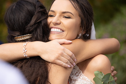 Wedding, bride and bridesmaid hug in celebration of marriage success, smile and bonding at outdoor venue. Friends, love and embrace in congratulations closeup of women celebrating at classy event