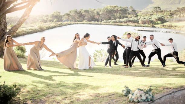 istock Wedding comedy, bride and groom party pulling, being funny and silly trying to separate married couple by a lake in nature. Happy men and women together for a marriage celebration together outside 1431987477