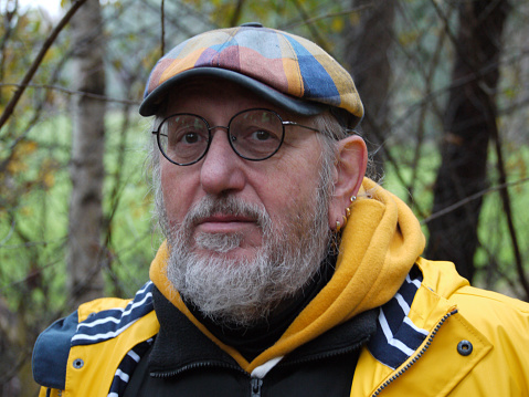 Man with is own feeling for taste. A yellow-blue checkered cap, yellow raincoat, earrings, yellowglasses and a beard. If he had been in his twenties, you'd call him a hipster.