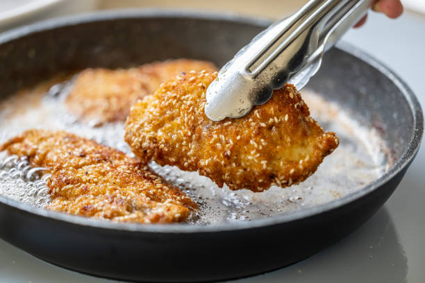 dettaglio delle pinze che prendono la cotoletta fritta da una padella sfrigolante. - viennese schnitzel foto e immagini stock