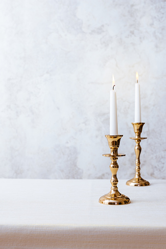 Cozy still life with burning candles in golden candlesticks on pastel light background. Concept Christmas Advent.