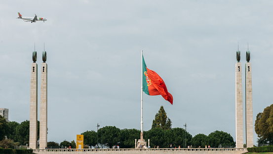 Lisbon, Portugal - October 9, 2022: Flag of Portugal at Eduardo VII Park juxta positioned against an aircraft belonging to TAP Portugal