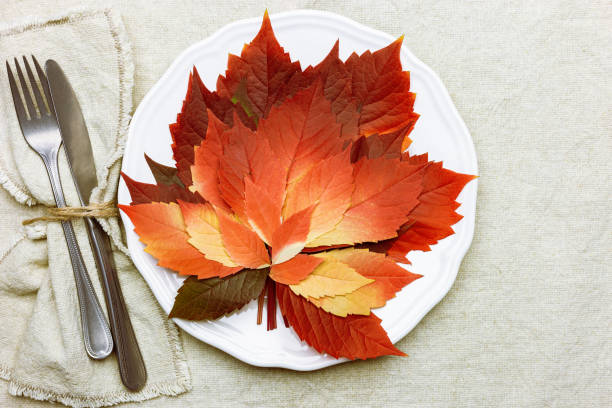 istock Autumn table setting, above view plate decorated red leaves and cutlery on coarse cotton tablecloth. Aesthetic autumn home and table decor. Fall season holiday decor from natural materials. 1431994054