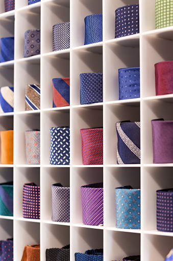 Showcase with multicolored ties. View of different colors ties in showcase. Showcase of rolled neckties at store. Twisted neckties are beautifully stacked in cells. Selective focus.