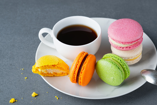 French colored macaroons with white cup of coffee on grey background.