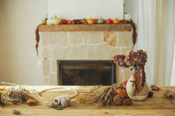 istock Making stylish autumn wreath on rustic table at fireplace. Fall decor and arrangement in farmhouse. Dried grass, hoop,  scissors, thread, pumpkins and candle on wooden table 1431998094