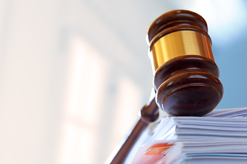 A gavel, photographed with a very shallow depth of field, rests on top of a stack of file folders and legal documents.