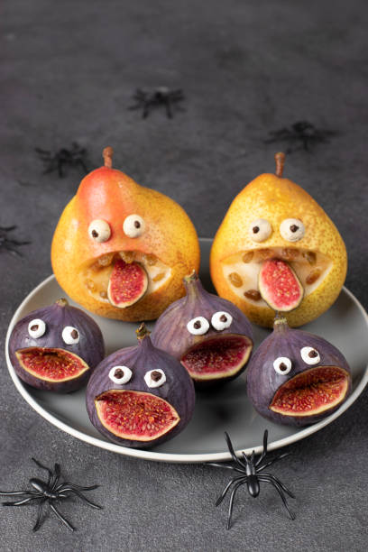 istock Spooky pear and fig monsters for Halloween party on gray background decorated with spiders and bats, Halloween Fruit Serving Idea 1432000936
