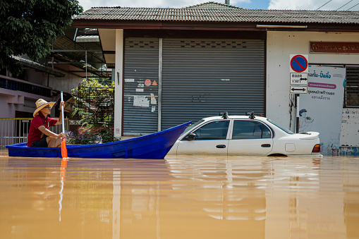 A woman girl in a boat next to a car as in a flooded street in Chiang Mai, Thailand.